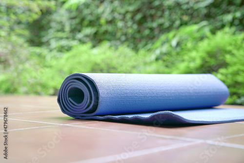 Blue color exercise mat for yoga on the floor against green plant background.