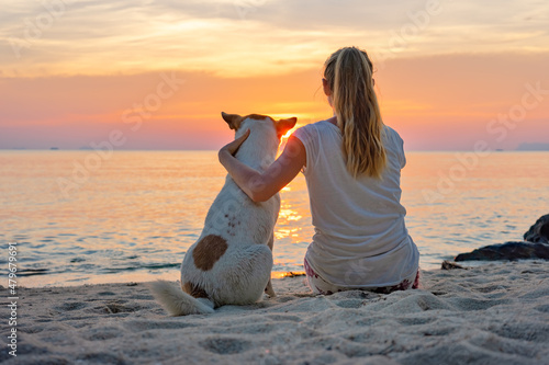 Young woman with dog sitting together on the beach and enjoying the sunset