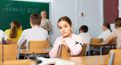 Teen girl listening to lecturer and writing in notebook in classroom
