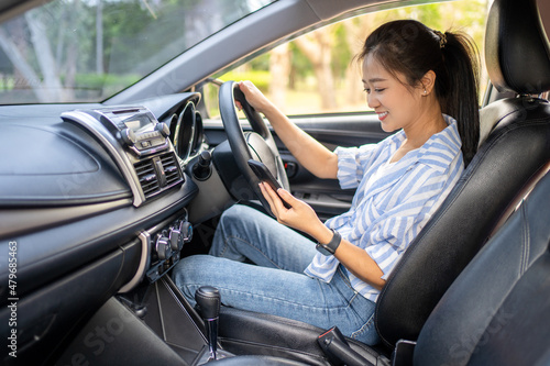 Portrait of a young woman texting on her smartphone while driving a car. Business woman sitting in car and using her smartphone. © PBXStudio