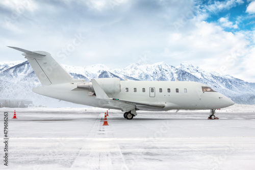 White luxury corporate business jet on the winter airport apron on the background of high scenic mountains