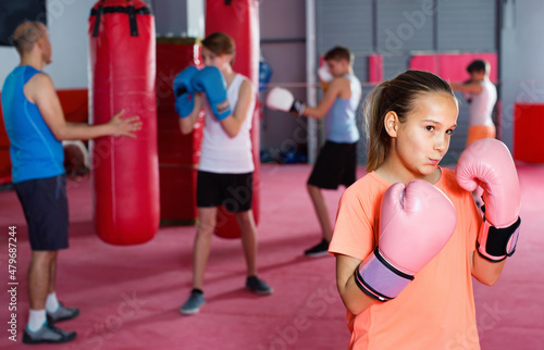 Young diligent girl in gloves posing during boxing training at gym
