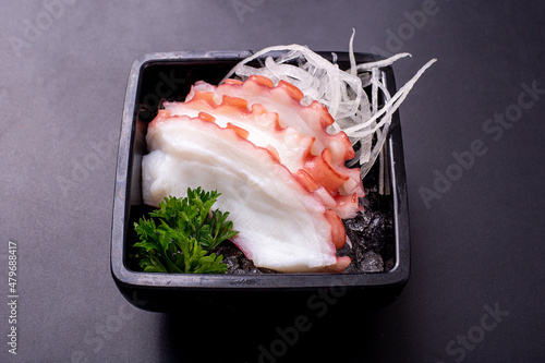 3 slices fresh squid sashimi and shredded radish put on ice in a black small dish. japanese food. photo
