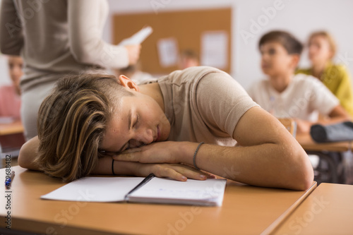 Tired bored teenage schoolboy sleeping at desk