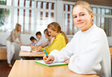 Teenage girl sitting at desk in classroom and looking at camera during lesson.
