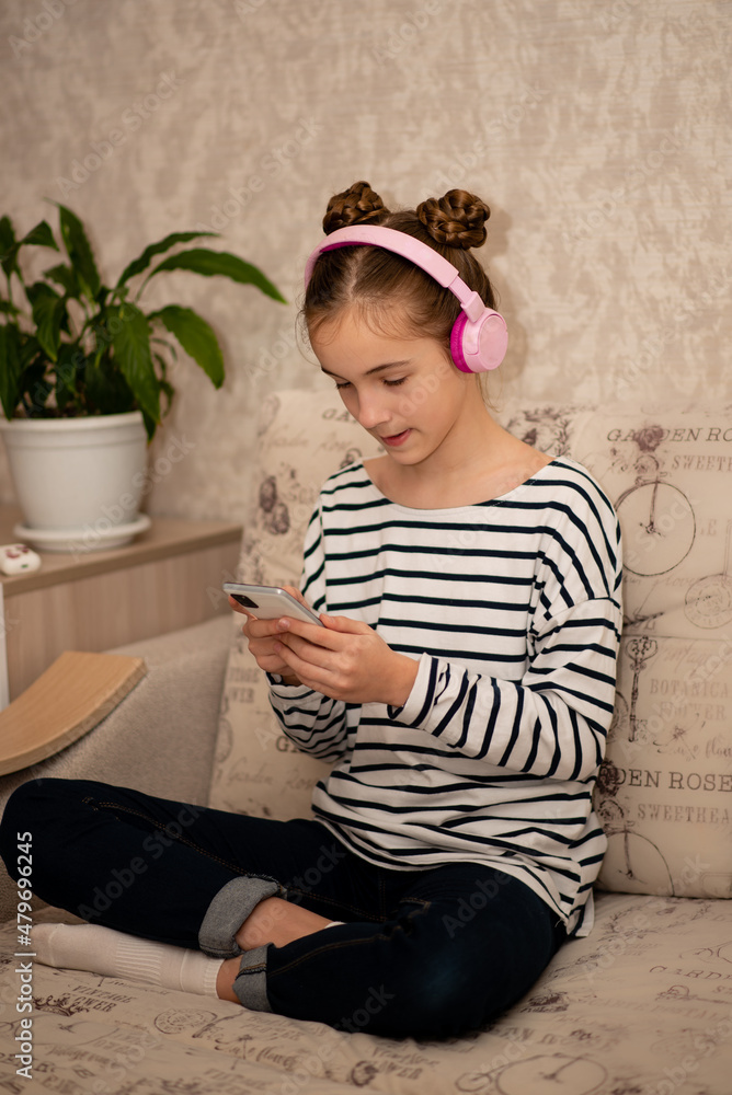 Fototapeta premium A cute teenage girl sits on the couch and chats online. Communication. Home.