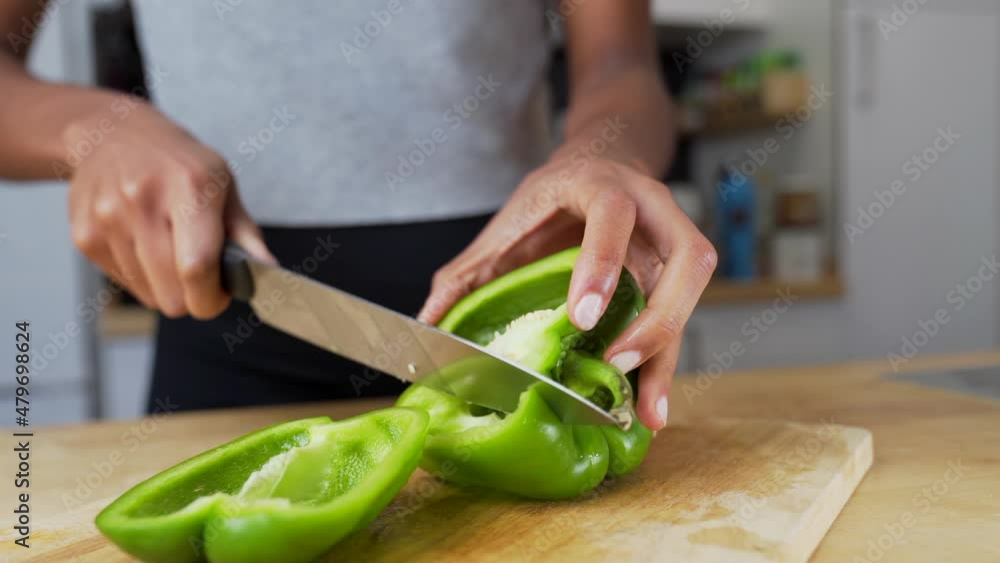 Dark-skinned woman cutting a green bell pepper into pieces on a wooden cutting board. Dark-skinned woman cutting a green bell pepper into pieces on a wooden cutting board.
