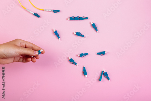 Hand takes blue LC optical attenuator on pink background photo