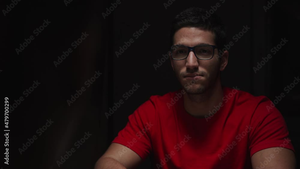 Medium shot of white young man sitting under noir lighting, man leaves, static Medium shot of white young man sitting under noir lighting, man leaves, static