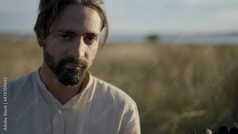 Bearded Spanish man playing guitar and singing by the river at sunset - face close-up Bearded Spanish man playing guitar and singing by the river at sunset - face close-up