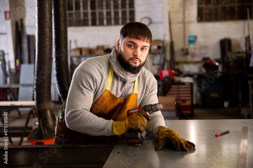 Serious young bearded locksmith posing in interior of small private workshop photo