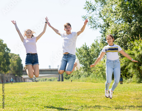 Three joyful teens jump on a spring lawn