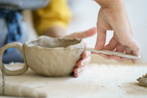 Professional ceramist at work using tools for creating handmade cup in studio, selective focus. Closeup of female potter hands shaping handcraft crockery in studio. Art and small business concept photo