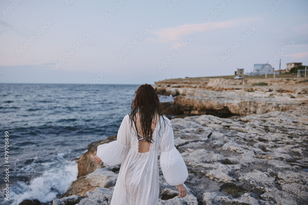 red-haired woman in white dress walking along the coast of the ocean rocks unaltered red-haired woman in white dress walking along the coast of the ocean rocks unaltered