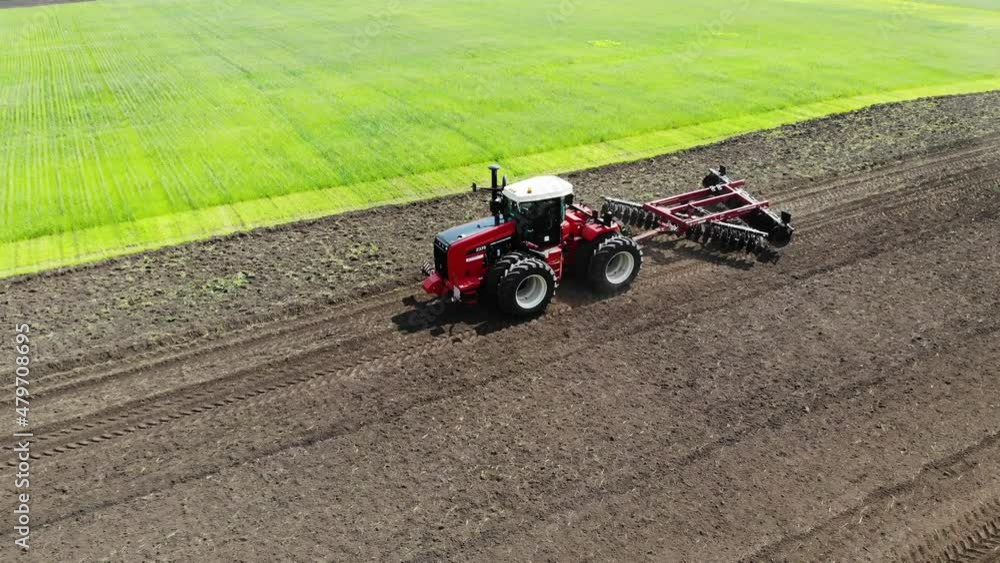 Red harvester drives across field and plows earth. Sows grain in field. He drives and leaves tracks in form of stripes. Russian field, harvesting, grain, agriculture, cultivation, modern technologies Red harvester drives across field and plows earth. Sows grain in field. He drives and leaves tracks in form of stripes. Russian field, harvesting, grain, agriculture, cultivation, modern technologies