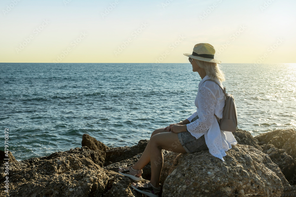 Mature woman traveler sitting by a beach at sunset.