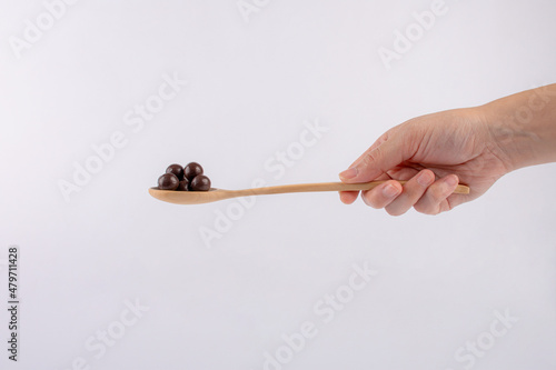 Hand and chocolate balls on wooden spoon on a white background.