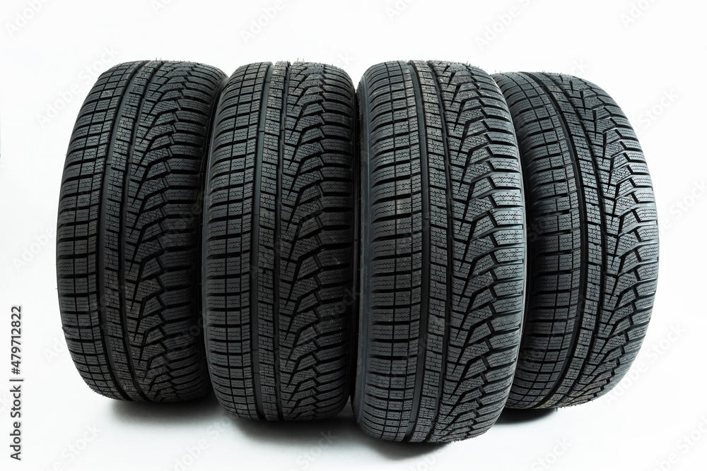 Winter tires rolling forward isolated on white background. Set of four wheel for use in snow and on ice with copy space. Deep pattern in rubber for transportation.