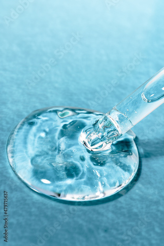 Liquid transparent gel and a glass pipette for research on a blue textured background. Cosmetic serum close-up. © Юлия Черкасова