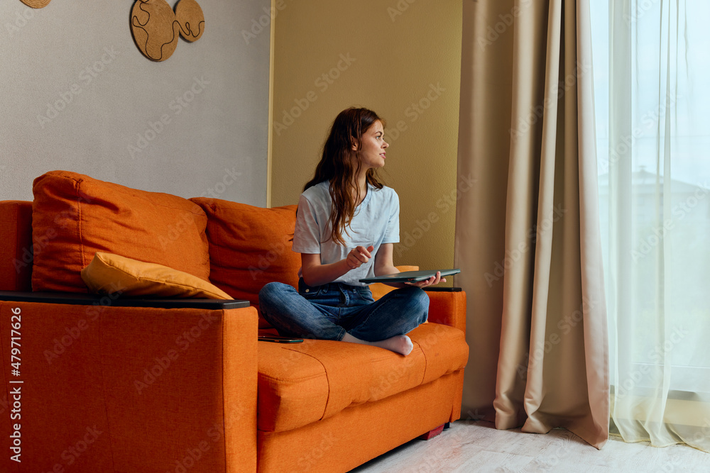 cheerful woman chatting on the orange couch with a laptop apartments cheerful woman chatting on the orange couch with a laptop apartments