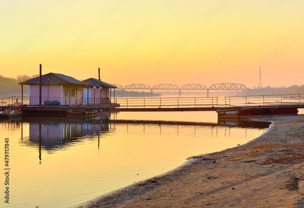 The bank of the Ob River. Sandy beach, boat pier, railway bridge on the horizon in the morning. Novosibirsk, Siberia, Russia, 2021