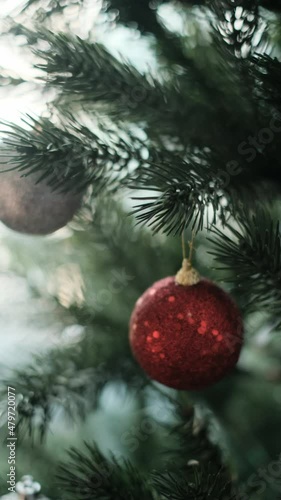 Close-up hands decorating Christmas tree with balls on the background of bright festive lights. Woman decorating a Christmas tree.