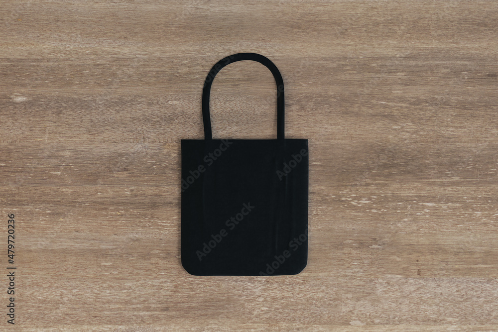 Fototapeta premium Top view and close up of empty black shopper on wooden table background. Mock up, advertisement, 3D Rendering.
