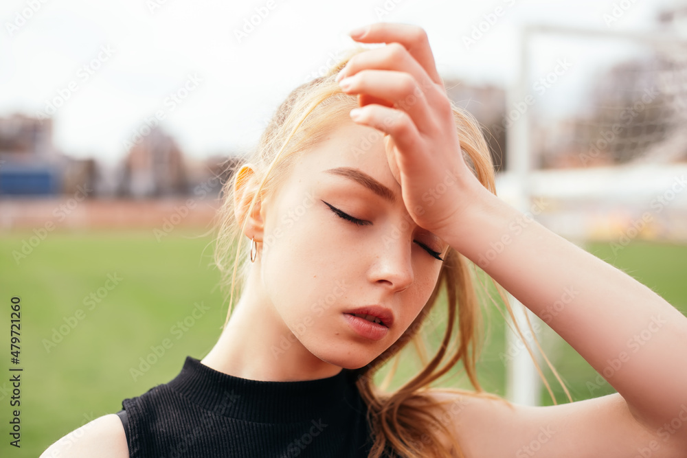 Woman standing on the football stadium with green grass or lawn. Lady tired exhausted after running treadmill productive workout, wipes off the sweat. Female dressed in sportswear.