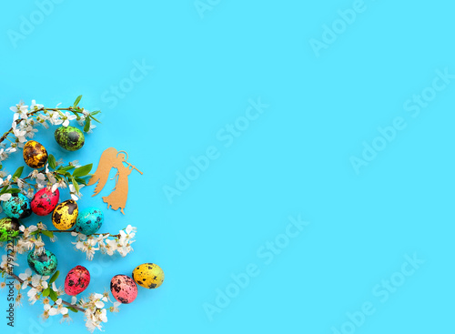 Easter colorful eggs, decorative angel and cherry flowers on blue background. Easter holiday concept. symbol of Christian holidays, spring festive decor. flat lay. copy space