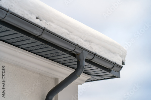 Konstfotografi Corner of house with new roof made of gray metal tiles and gutter covered with thick layer of snow in winter