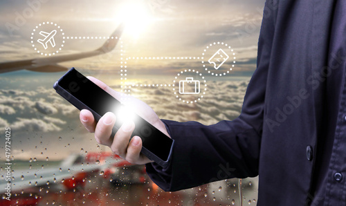 Business man hold smartphone in hand with luggae travel ticket icon in concept of smart travel technology with airport and airplane wing fly over cloud sky background landscape photo