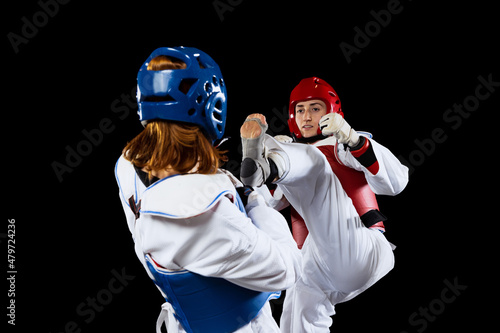 Close-up two young women, taekwondo athletes training together isolated over dark background. Concept of sport, skills