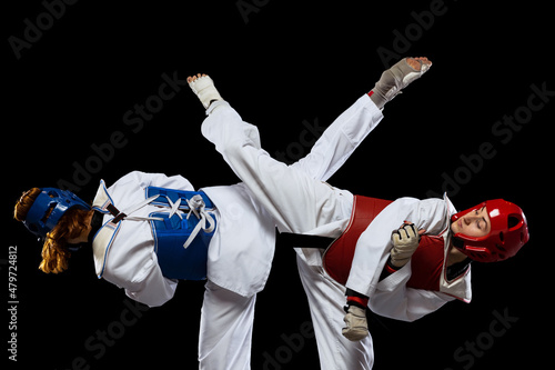 Two young women, taekwondo athletes wearing sports uniform practicing isolated over dark background. Concept of sport, skills photo