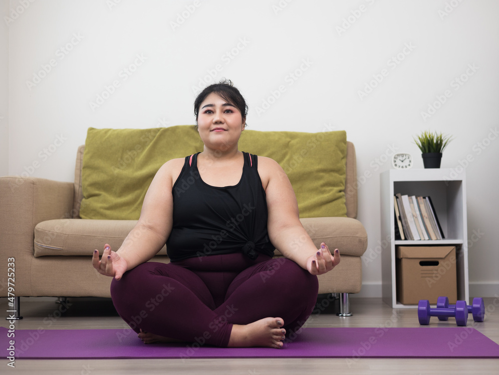 Young asian sport woman plus size sitting on the yoga mat practicing meditation. Fitness or exercise at home. Beautiful female relaxing after workout. Young asian sport woman plus size sitting on the yoga mat practicing meditation. Fitness or exercise at home. Beautiful female relaxing after workout.