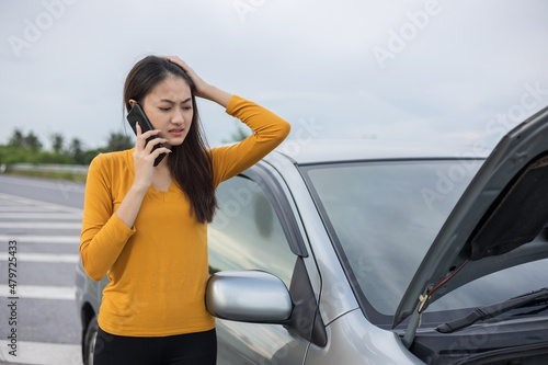 Young asian woman has broken down car on the road she feeling serious and stressed. Look for someone help. Using smartphone Call Emergency assistance or insurance service. © Chanakon