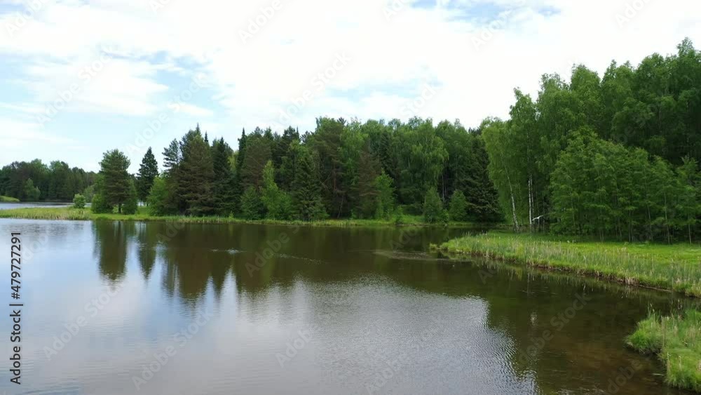 Low altitude aerial 4K drone shot of calm tranquil lake. River water landscape with forest around. White clouds mirroring on water surface. Low altitude aerial 4K drone shot of calm tranquil lake. River water landscape with forest around. White clouds mirroring on water surface.