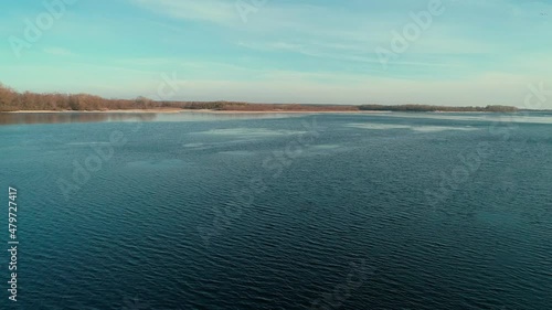 Aerial drone footag of flying over a calm river in winter forest in the distance photo