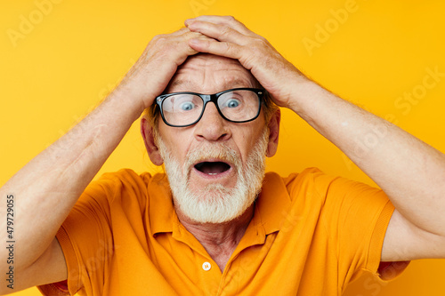 Senior grey-haired man posing yellow tshirt glasses yellow background