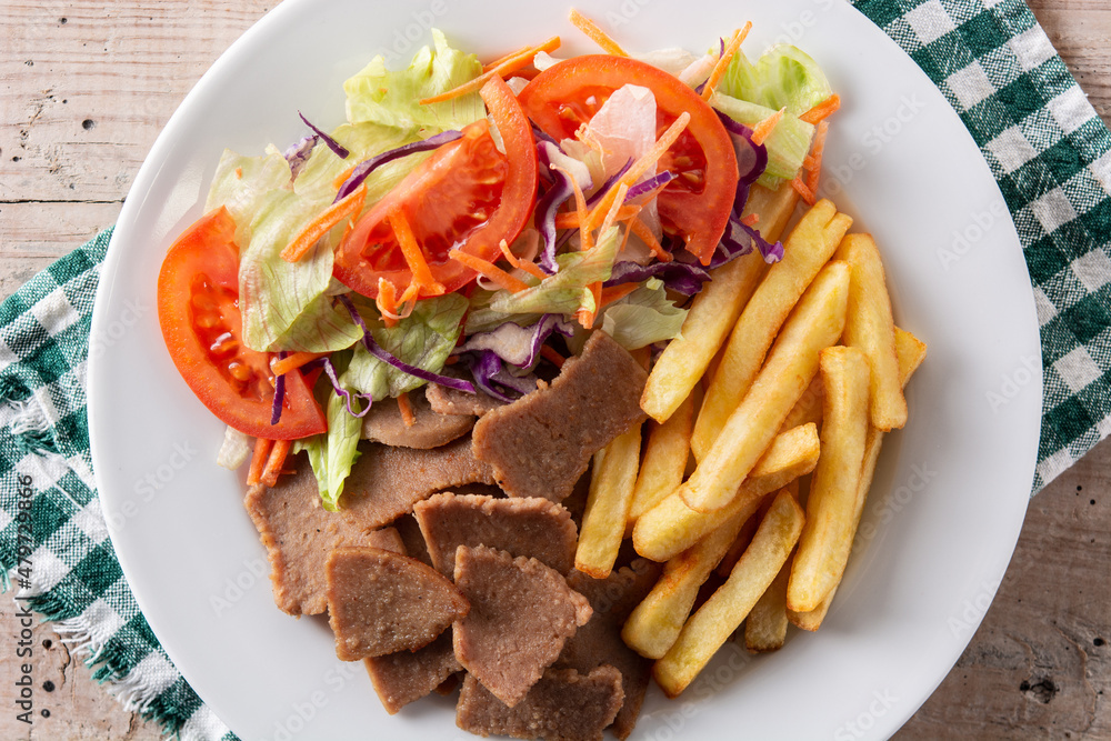 Plate of kebab, vegetables and french fries on wooden table Plate of kebab, vegetables and french fries on wooden table