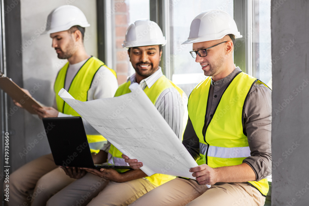 architecture, construction business and people concept - group of male architects in helmets with laptop, blueprint and clipboard working at office architecture, construction business and people concept - group of male architects in helmets with laptop, blueprint and clipboard working at office