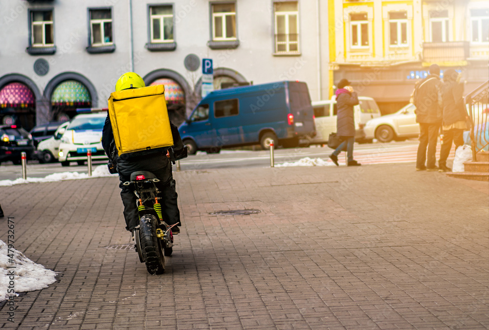 Food delivery driver with yellow backpack on a motorcycle riding along a street