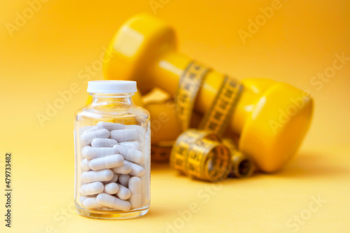 Pills capsules in a glass jar with dumbbells and a centimeter tape in the background. The concept of weight loss, sports, fitness, fat burner, vitamins, sports nutrition.