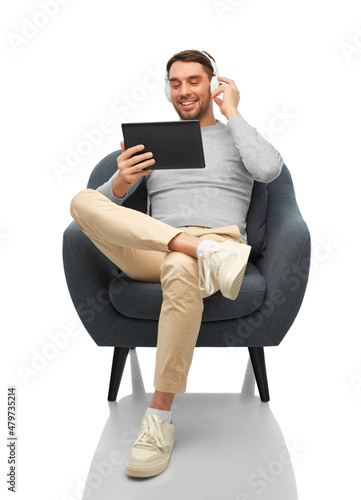 people, technology and music concept - happy smiling man with headphones and tablet pc computer sitting in chair over white background