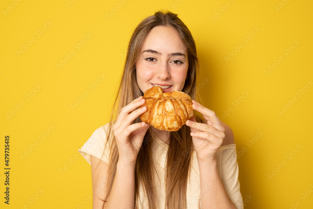 Young woman eating croissant, coffee break. Isolated over yellow background. Diet concept. Young woman eating croissant, coffee break. Isolated over yellow background. Diet concept.