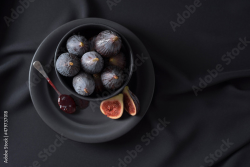 Higos negros y una cuchara con mermelada de higos en un plato negro sobre fondo oscuro. Vista superior photo