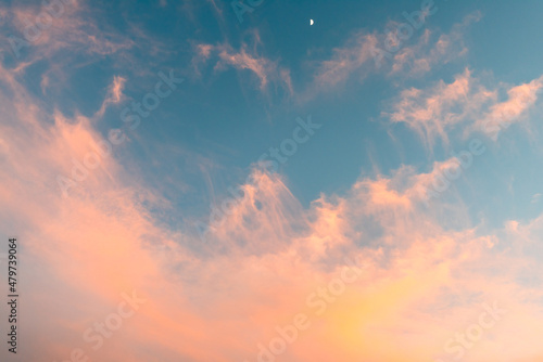 Big cirrus clouds with sunset colors on a blue sky with half moon in the top.