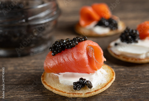 Salmon and black sturgeon caviar on blini pancakes on a wooden table close-up photo