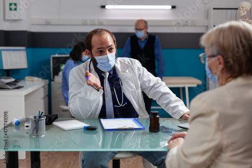 General practitioner doing medical consultation with senior woman during coronavirus pandemic. Medic and patient with face mask meeting in health care office to do checkup examination.