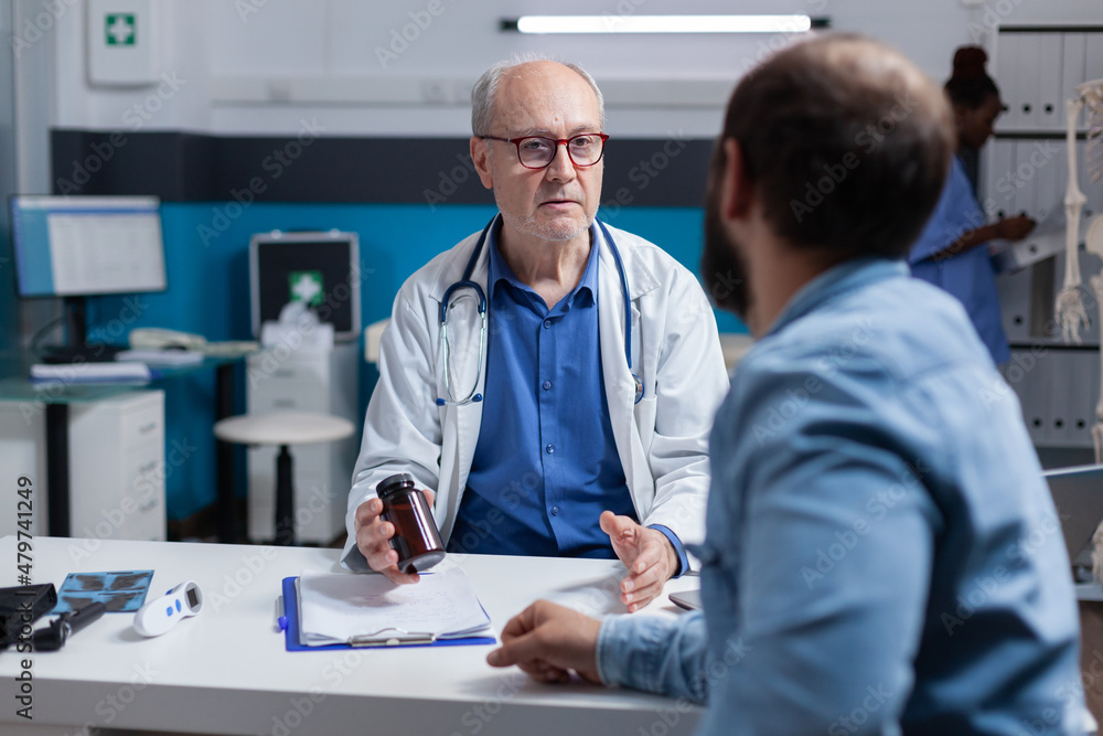 Fototapeta premium Physician showing bottle of pills to young man at consultation appointment, giving jar with medicine to cure illness. General practitioner holding healthcare treatment for patient.
