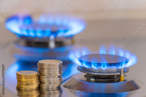 Gas stove lit, with stacks of coins above it. Increase in gas costs and tariffs. 